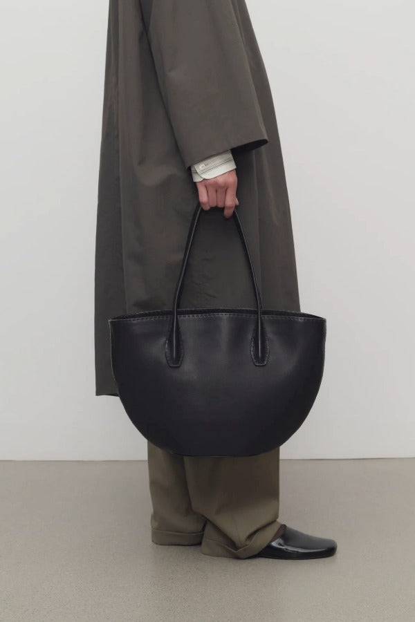 Front view of black alger tote on model wearing khaki pants, dark green coat, and loafers against a white background.