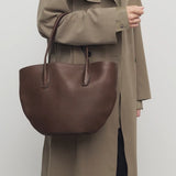 Front view of deep brown alger tote on model wearing beige trench coat, against a white background.