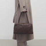 Front view of brown astra bowling bag on model wearing taupe trench coat pants an ballet flats, against a white background.