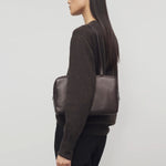 Front view of dark brown astra bowling bag on. model wearing brown sweater and black pants, against a white background.