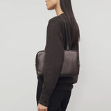 Front view of dark brown astra bowling bag on. model wearing brown sweater and black pants, against a white background.