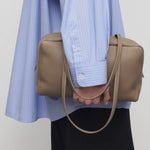 Alternate front view of smoke taupe astra bowling bag on model wearing blue shirt and black pants, against a white background.