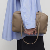 Alternate front view of smoke taupe astra bowling bag on model wearing blue shirt and black pants, against a white background.