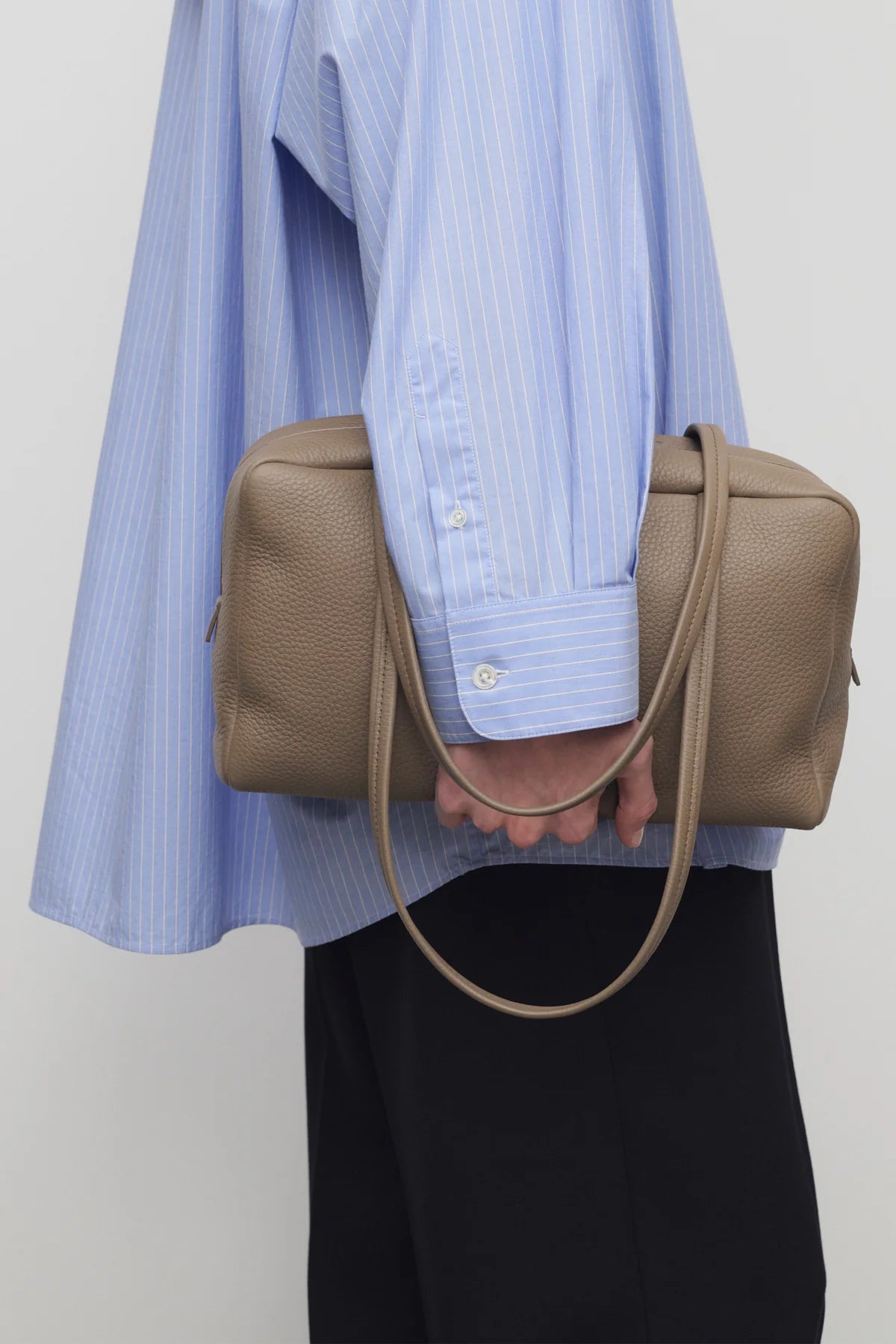 Front view of smoked taupe astra bowling bag on model wearing blue shirt and black pants against a white background.
