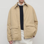 Front view of sand aurelius jacket on model wearing black sweater, white shirt and pants, against a white background.