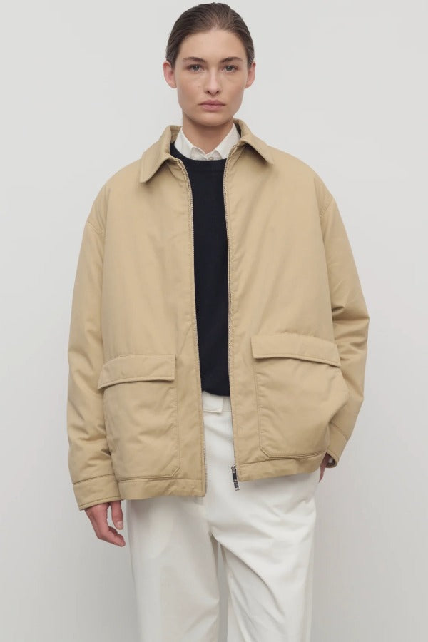 Front view of sand aurelius jacket on model wearing black sweater, white shirt and pants, against a white background.