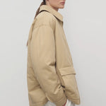 Side view of sand aurelius jacket on model wearing white pants, against a white background.