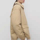 Side view of sand aurelius jacket on model wearing white pants, against a white background.
