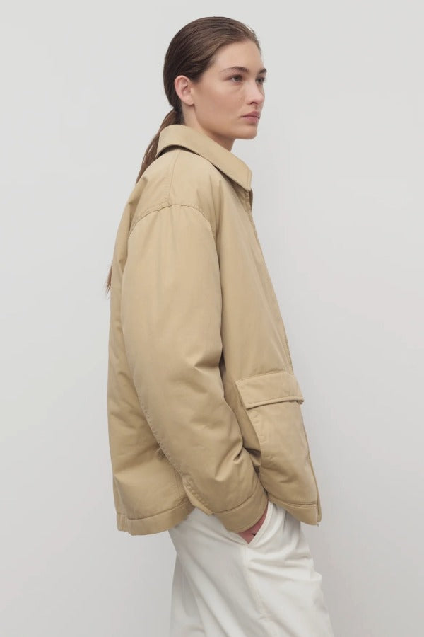 Side view of sand aurelius jacket on model wearing white pants, against a white background.