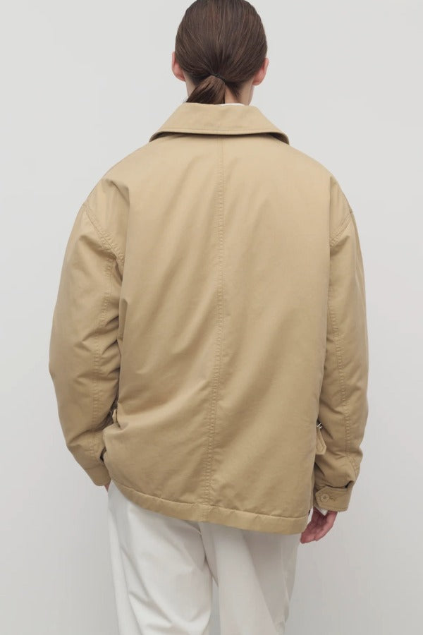 Back view of sand aurelius jacket on model wearing white pants, against a white background.