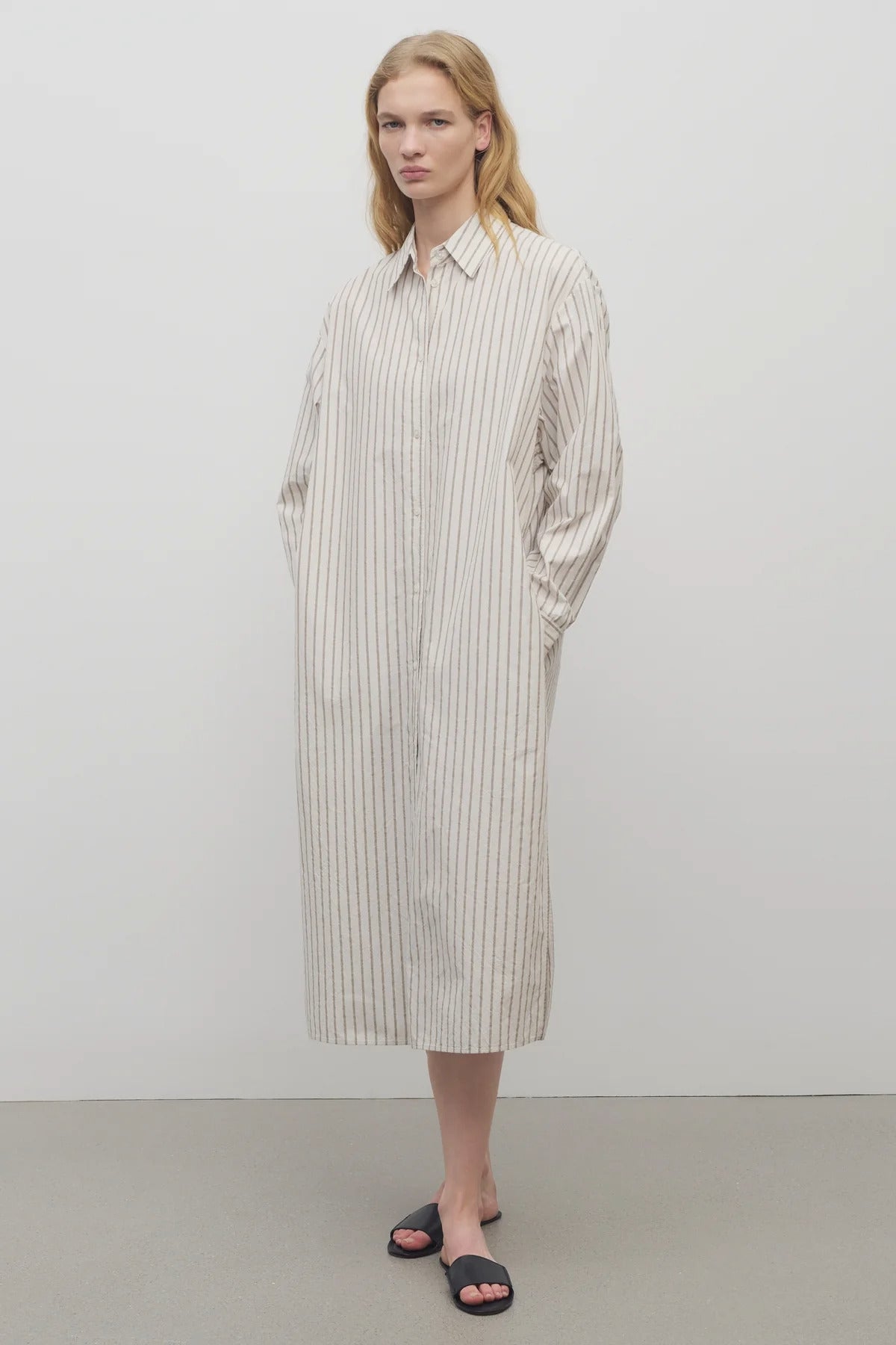 A blonde model standing at a front view in the midi dress with white background.