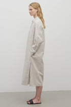 A blonde model standing at a side view in the midi dress with white background.