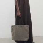 Front view of a mesh and leather blue bag pictured on a white background, with model wearing brown dress and ballet flats.