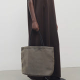 Front view of a mesh and leather blue bag pictured on a white background, with model wearing brown dress and ballet flats.