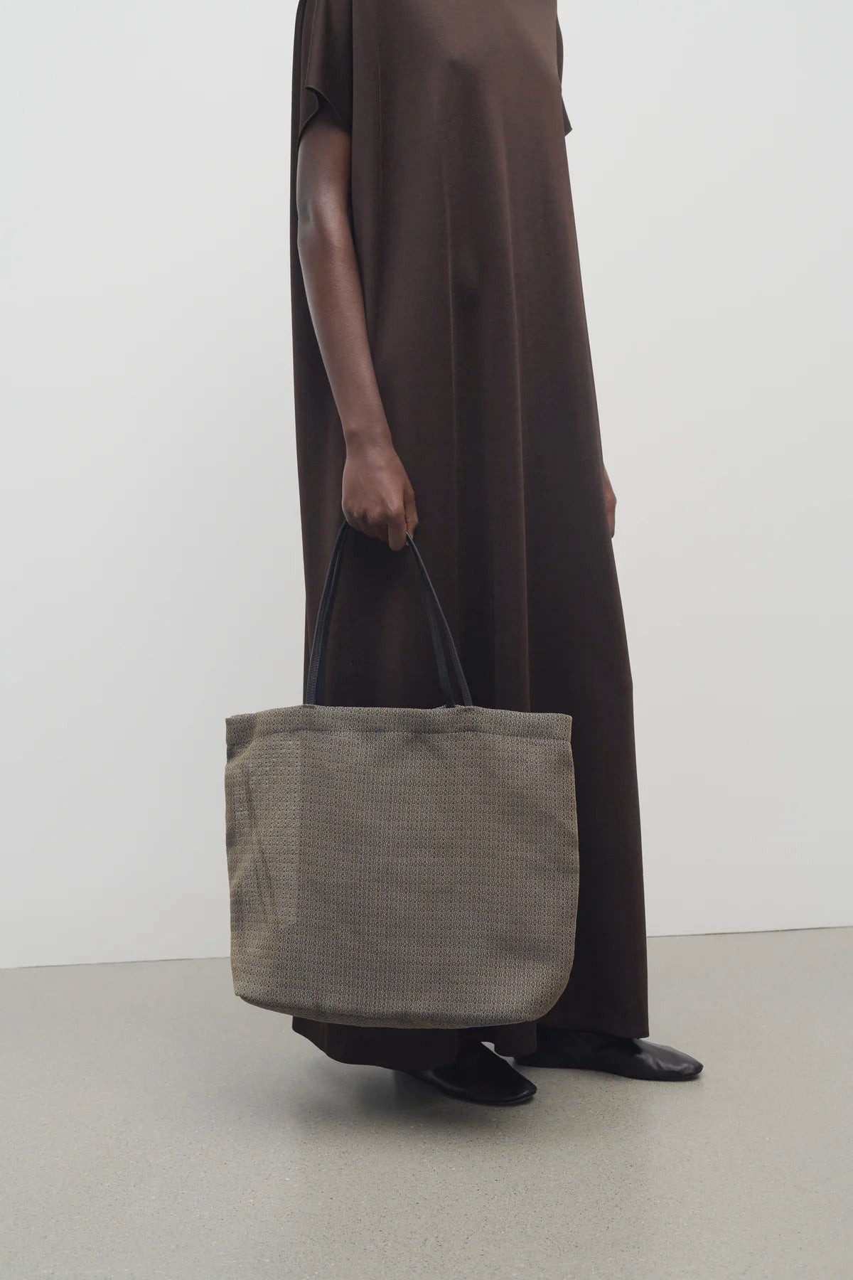 Front view of a mesh and leather blue bag pictured on a white background, with model wearing brown dress and ballet flats.