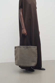 Front view of a mesh and leather blue bag pictured on a white background, with model wearing brown dress and ballet flats.