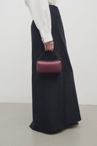 Front view of a purple leather bag on a white background, with model wearing dark long skirt and white blouse.