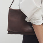 Front view of brown melange nan shoulder bag on model wearing white collar shirt with black trousers, against a white background.