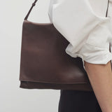 Front view of brown melange nan shoulder bag on model wearing white collar shirt with black trousers, against a white background.