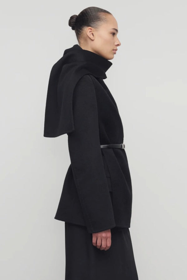 Side view of black calitra jacket on model wearing black skirt, against a white background