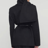 Back view of black calitra jacket on model wearing black skirt, against a white background.
