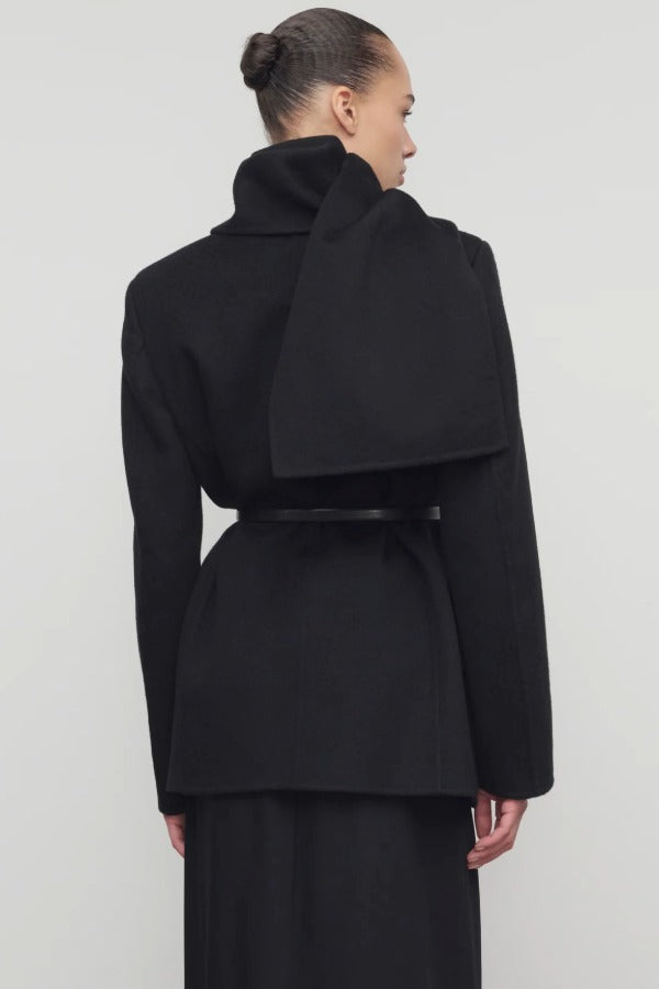 Back view of black calitra jacket on model wearing black skirt, against a white background.