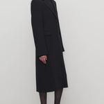 Side view of black cerys coat on model wearing black heels, against a white background.