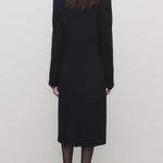 Back view of black cerys coat on model wearing black heels, against a white background.