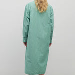 Long blond-haired model wears long-sleeved green with white button-down midi dress and black sandals. Back viewpoint with white background.