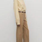 Side view of anise clair pant on model wearing yellow shirt and mules, against a white background.