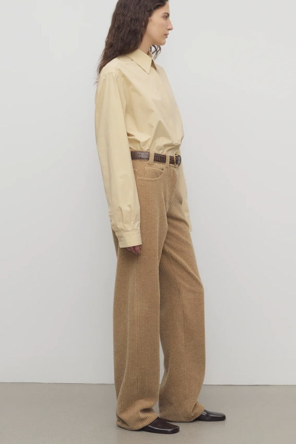 Side view of anise clair pant on model wearing yellow shirt and mules, against a white background.