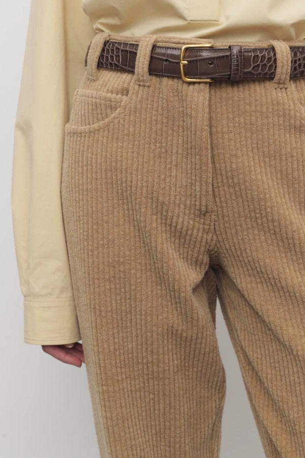 Front closeup view of anise clair pant on model wearing yellow shirt and brown belt, against a white background.