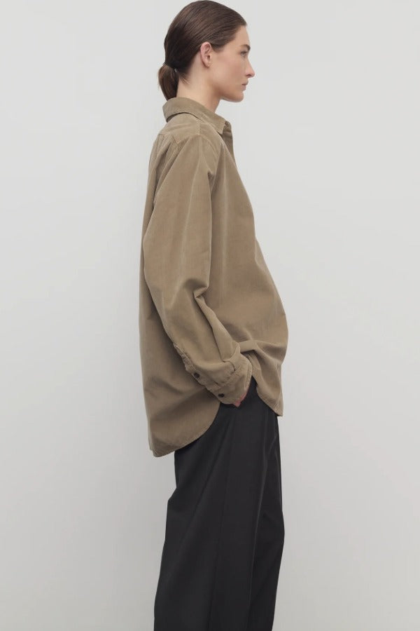 Side view of beige corduroy sisilia shirt on model wearing grey pants, against a white background