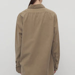 Back view of beige corduroy sisilia shirt on model wearing grey pants, against a white background.