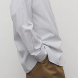 Side view of blue/white cotton sisilia shirt on model wearing camel trousers, against a white background.