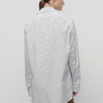 Back view of blue/white sisilia shirt on model wearing camel trousers, against a white backgorund,