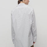 Back view of blue/white sisilia shirt on model wearing camel trousers, against a white backgorund,