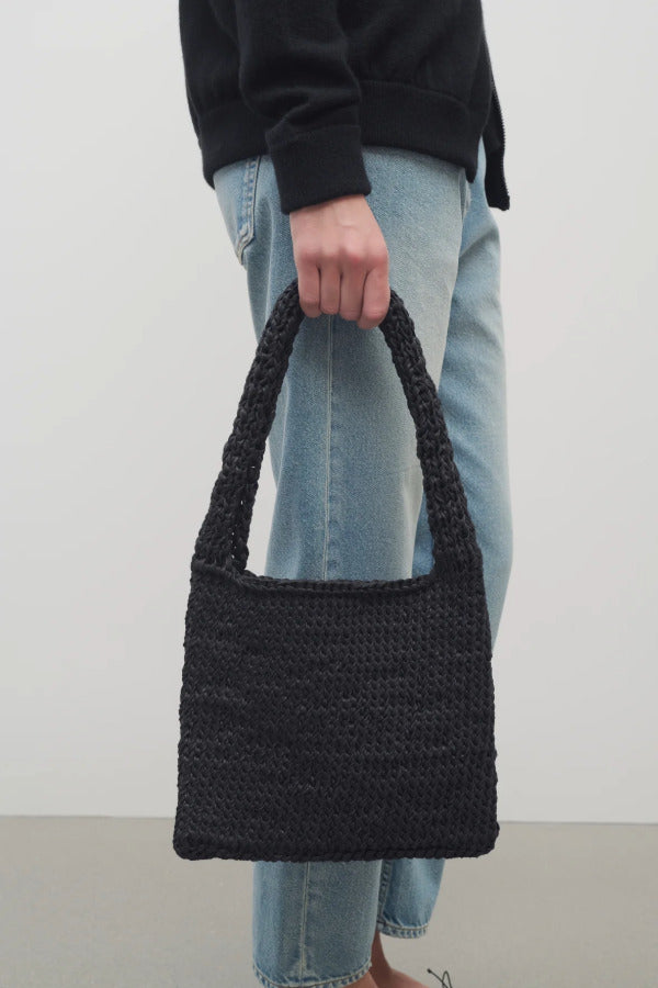 Front view of black Didion Shoulder bag on model wearing light-colored jeans and a black sweater, on a white background.