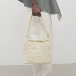 Front view of ivory didion shoulder bag on model wearing white pants with grey sweater, against a white background.