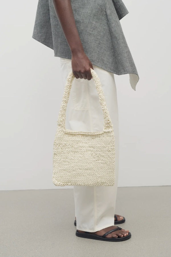 Front view of ivory didion shoulder bag on model wearing white pants with grey sweater, against a white background.