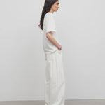 Side view of white eglitta jean on model wearing white t-shirt and sneakers, against a white background.