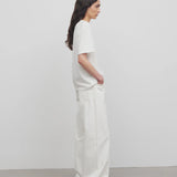 Side view of white eglitta jean on model wearing white t-shirt and sneakers, against a white background.