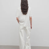 Back view of white eglitta jean on model wearing white t-shirt, against a white background.