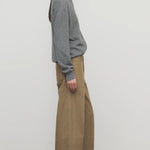 Side view of beige eglitta pant on model wearing grey sweater and boots, against a white background.
