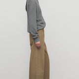 Side view of beige eglitta pant on model wearing grey sweater and boots, against a white background.
