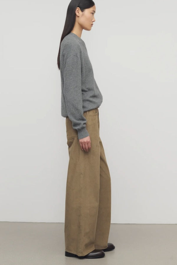 Side view of beige eglitta pant on model wearing grey sweater and boots, against a white background.