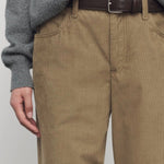 Front closeup of beige eglitta pant on model wearing grey sweater and brown belt, against a white background.