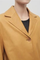 Closeup of the model wearing a caramel-colored leather button-down jacket with crew neck black undershirt.