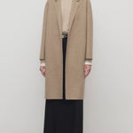 Front view of natural fedra coat on model wearing beige top, black skirt and mules, against a white background.