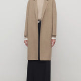 Front view of natural fedra coat on model wearing beige top, black skirt and mules, against a white background.
